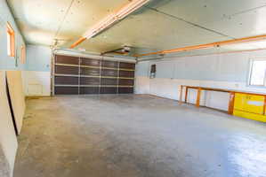 Spacious garage featuring a concrete floor, an overhead sectional garage door, exposed ceiling joists, and natural light from multiple windows