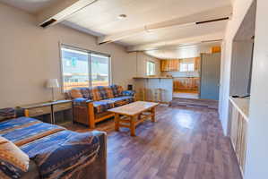 Open-concept living space featuring wood-finish flooring, exposed ceiling beams, and a built-in entertainment niche with wood paneling