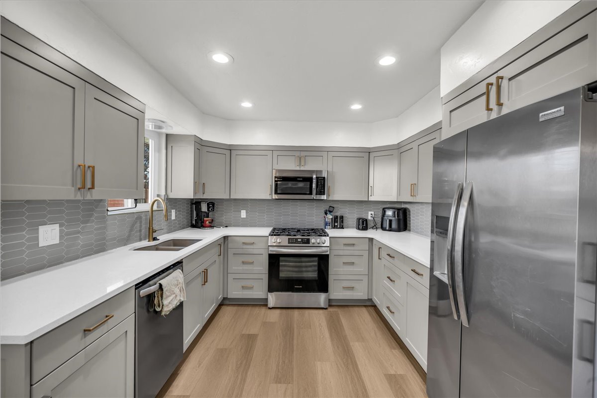 U-shaped kitchen featuring light gray cabinetry with gold-tone hardware, white countertops, and a gray geometric tile backsplash