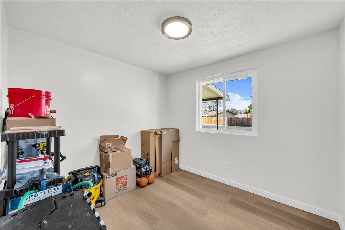 Bright interior room with white painted walls, wood-finish flooring, and a single window