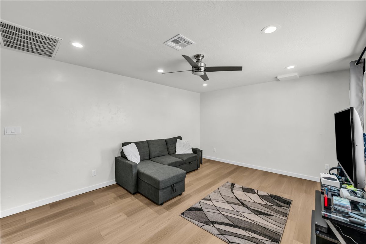Spacious room with wood-finish flooring, recessed lighting, a ceiling fan with brushed nickel accents, and white baseboards
