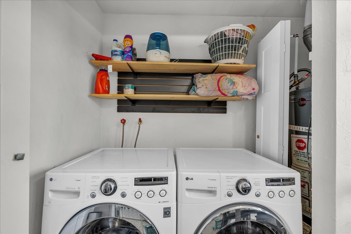 Dedicated laundry area featuring a front-loading washer and dryer, wall-mounted wooden shelving, and a water heater enclosure