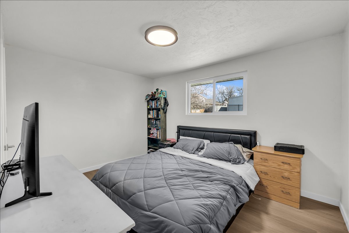 Bedroom featuring wood-finish flooring, a contemporary flush-mount ceiling light, white walls, a single window with white trim, and white baseboards