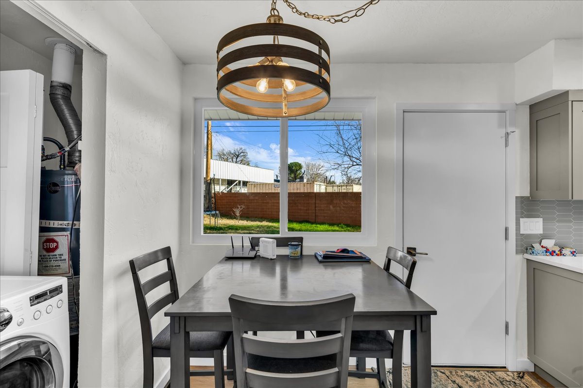 Bright dining area featuring a modern drum chandelier with exposed bulbs, a large window, and light gray cabinetry with a geometric tile backsplash