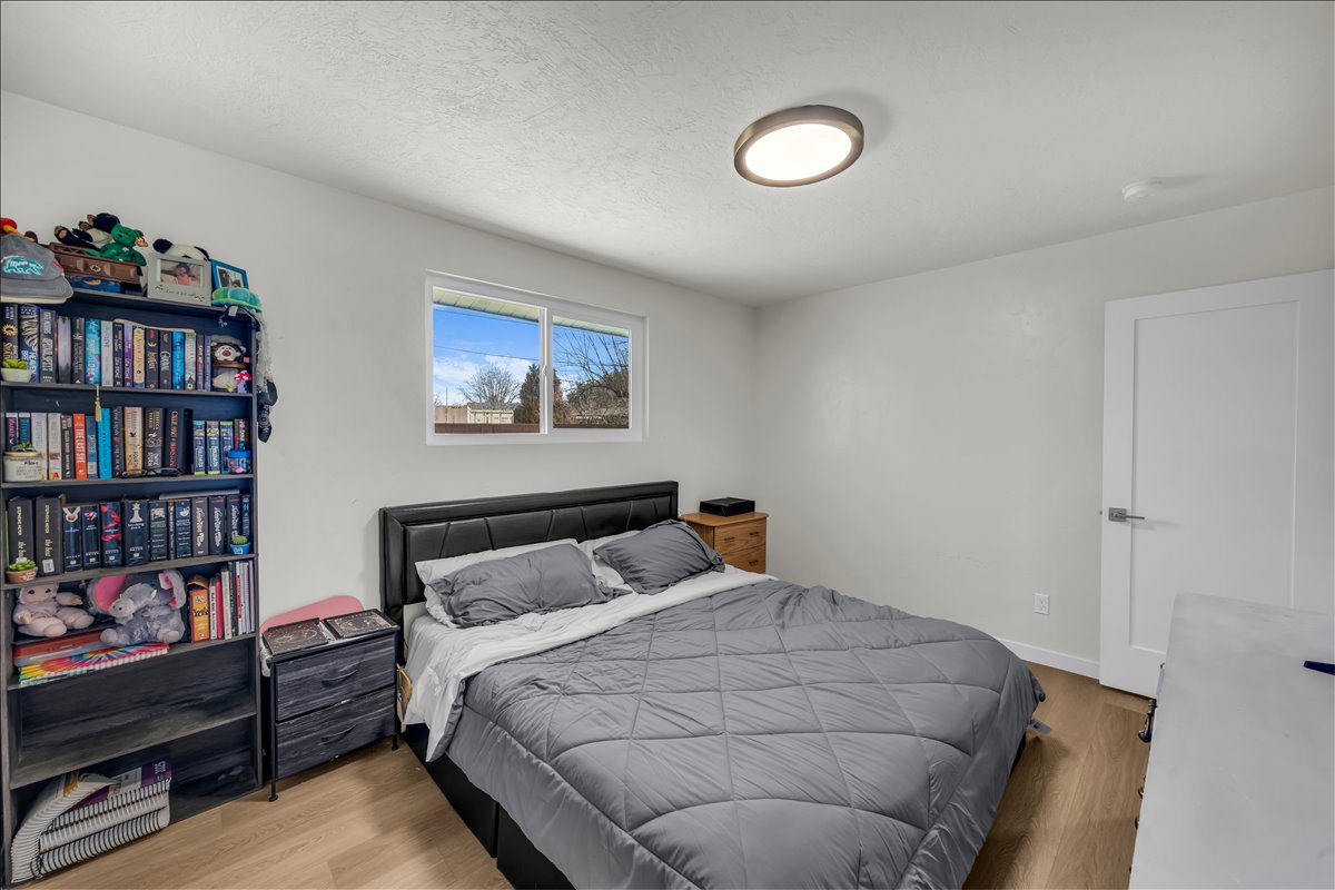 Bedroom featuring wood-finish flooring, a white interior door with contemporary hardware, a flush-mount ceiling light fixture, and a window with a white frame
