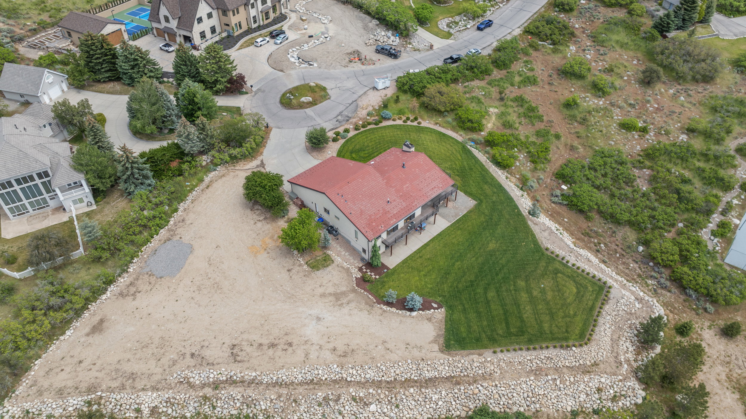 Expansive property featuring a red-roofed residence, a terraced lawn, and a spacious deck
