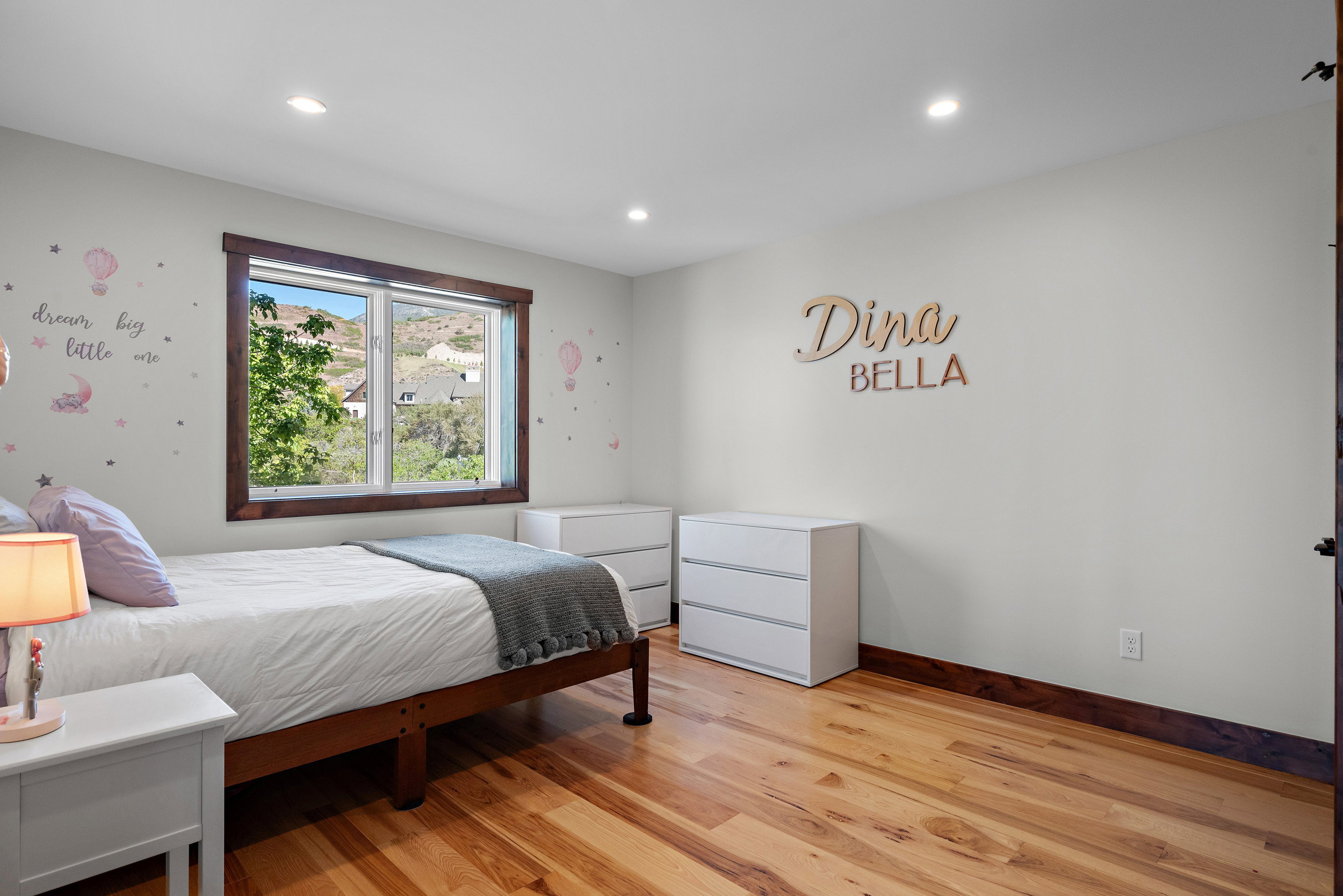 Bright interior space featuring light-toned walls, recessed lighting, wood-finish flooring, and a large window with dark wood trim overlooking distant hillsides