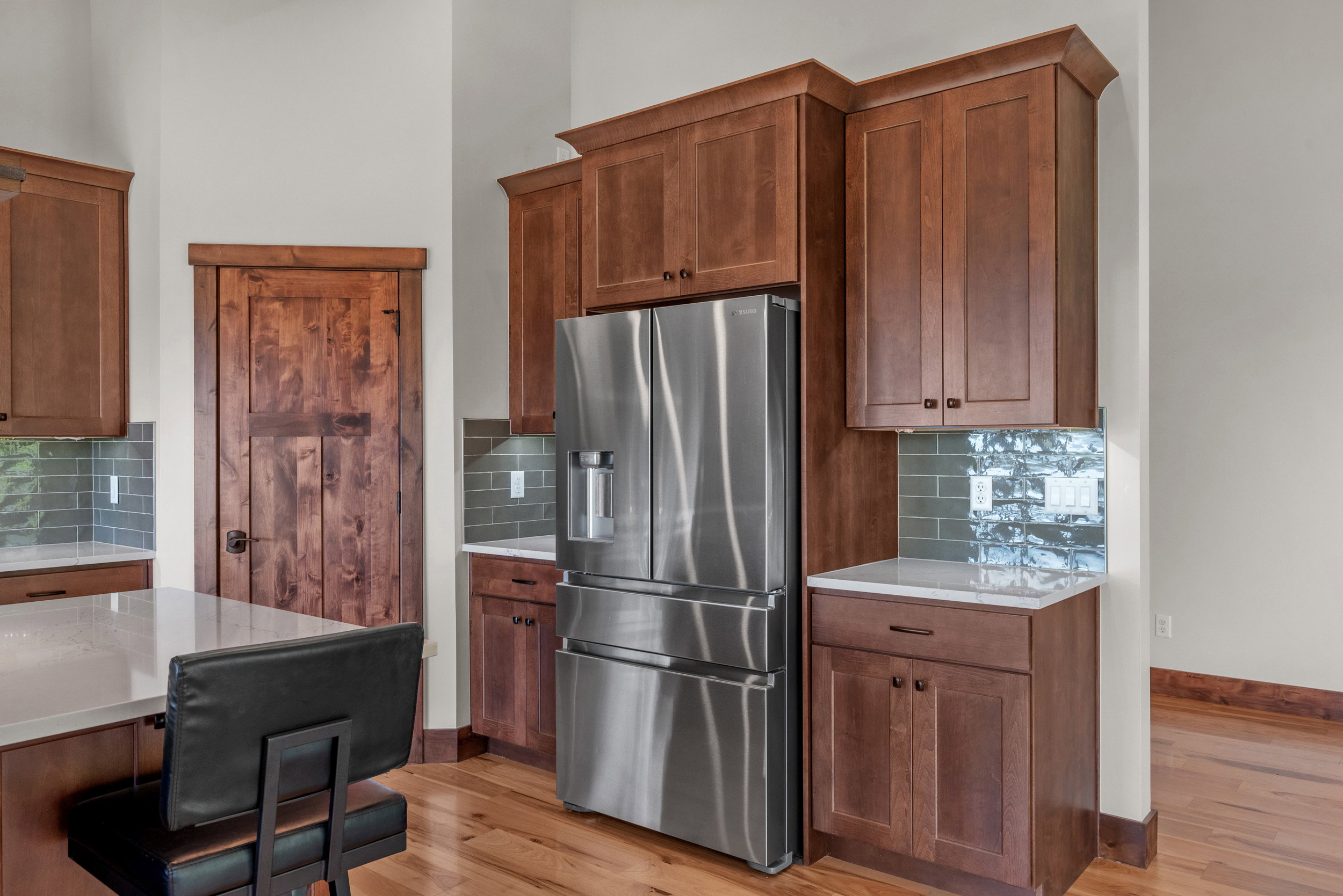 Gourmet kitchen featuring a stainless steel French door refrigerator, extensive wood cabinetry, light-toned countertops, and a tiled backsplash