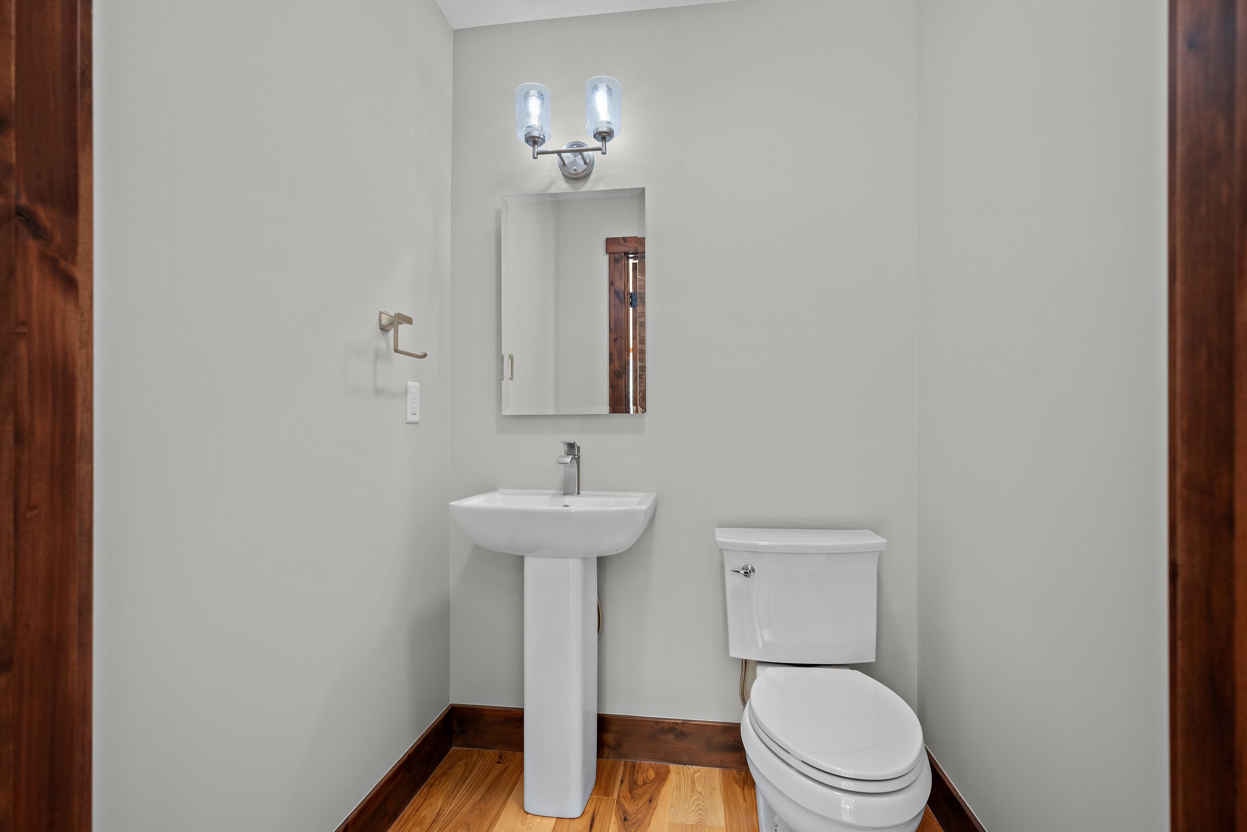 Pedestal sink with a single-handle faucet, rectangular mirror, and an overhead vanity light fixture