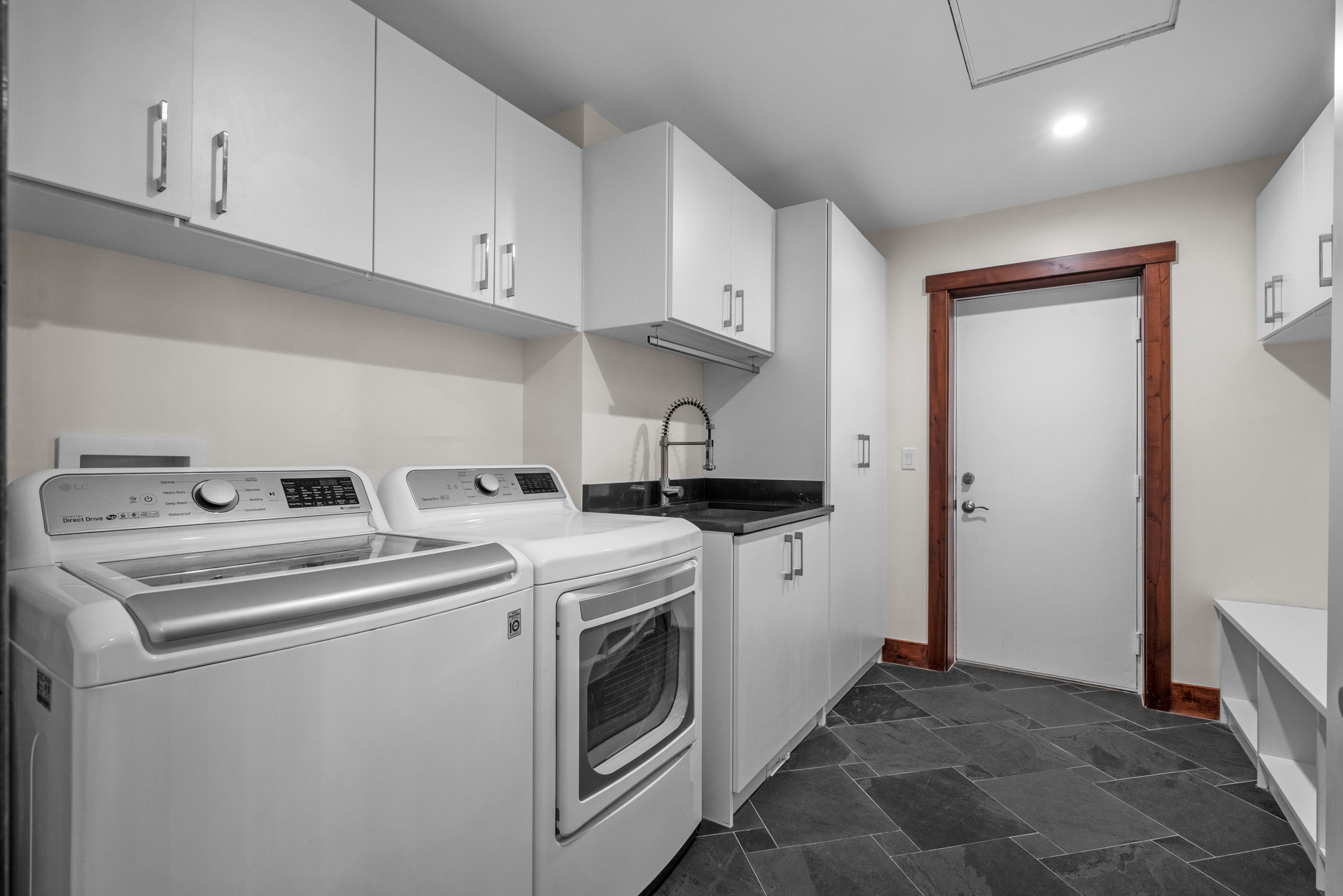 Laundry room featuring dark slate tile flooring, white cabinetry, a utility sink with a black countertop, and a wood-trimmed doorway