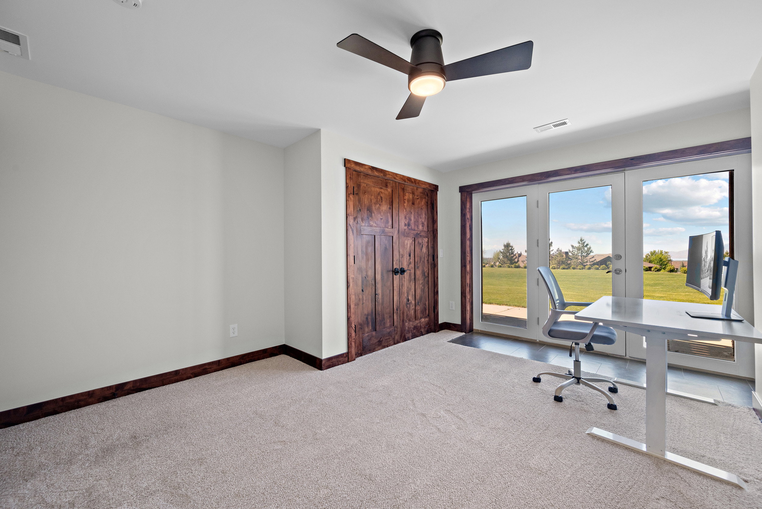 French doors opening to a green landscape, complemented by a ceiling fan with integrated lighting and a wood-paneled door