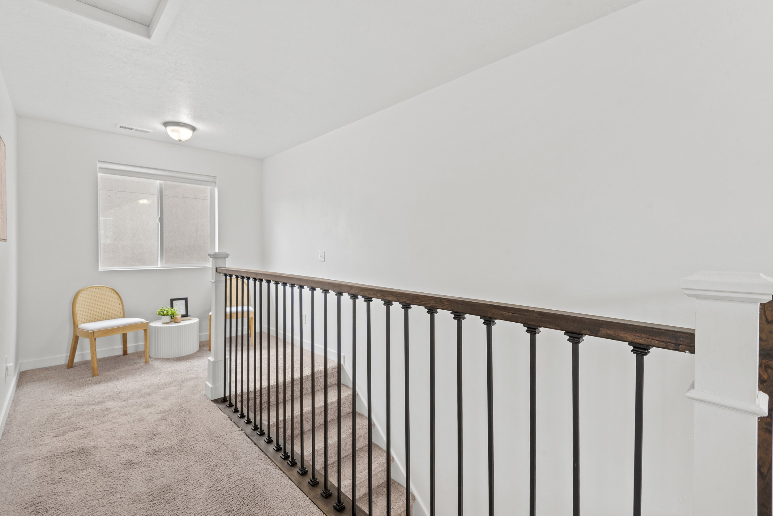 Carpeted hallway featuring a window with blinds, a flush mount light fixture, and a staircase with dark wood railing and black balusters