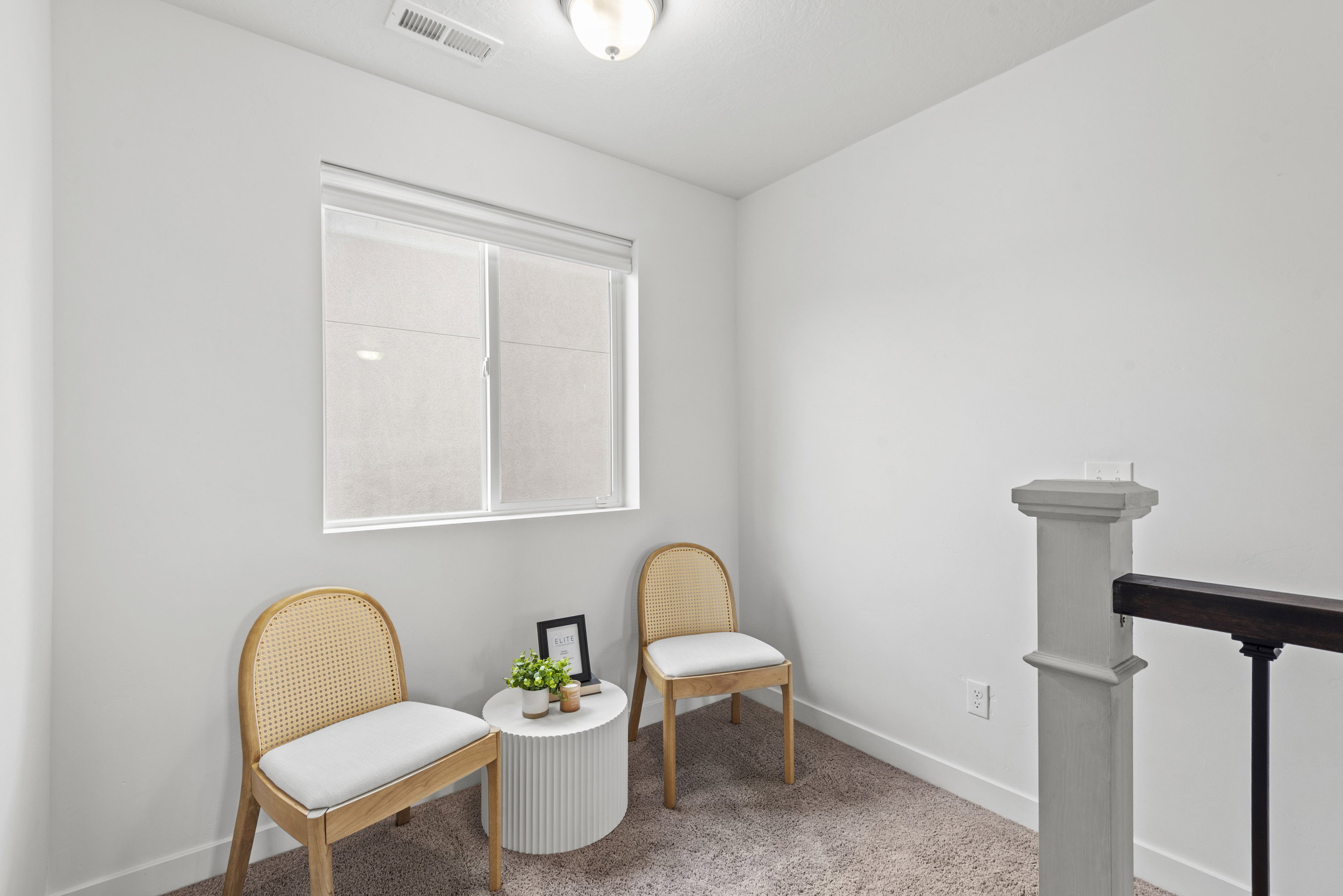 Bright interior space featuring a window with roller shades, neutral carpeting, white baseboards, and a contemporary ceiling light fixture