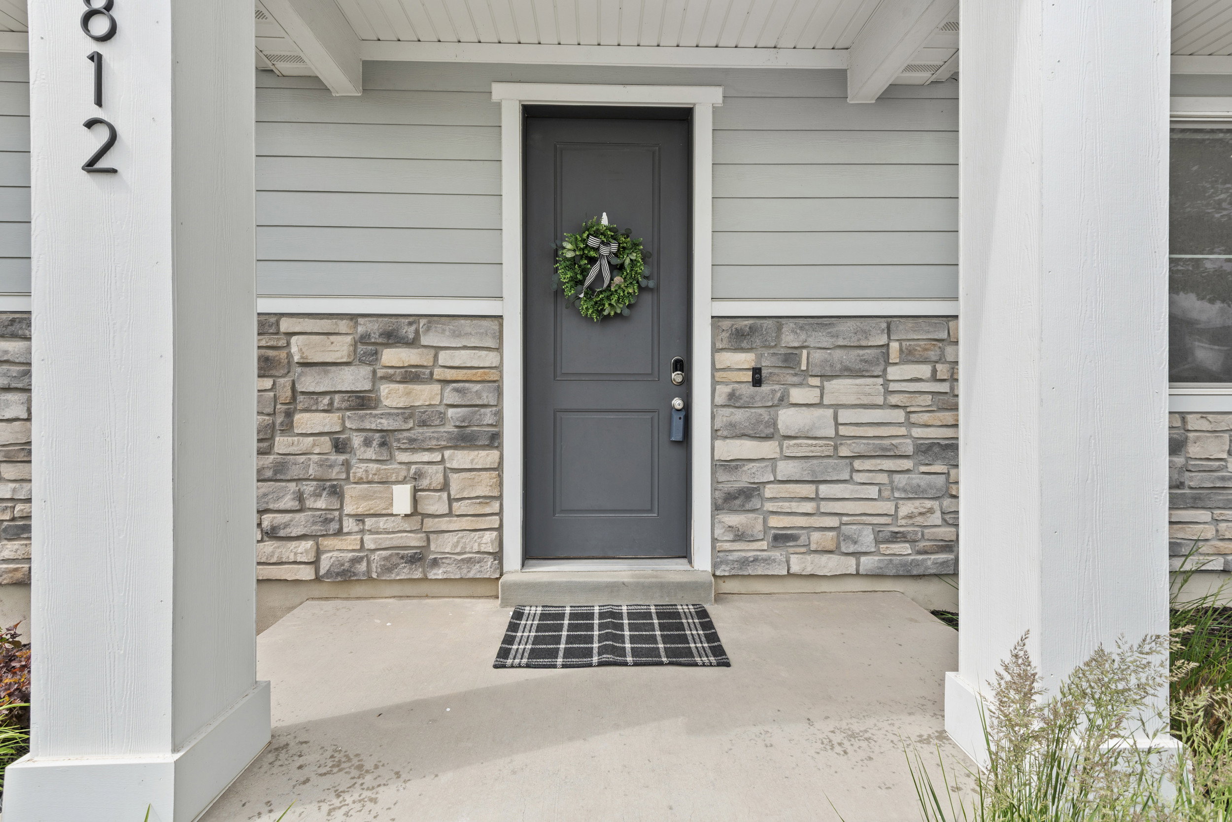 Exterior entry featuring a dark gray paneled door with smart lock hardware, light gray horizontal siding, and natural stone veneer accents