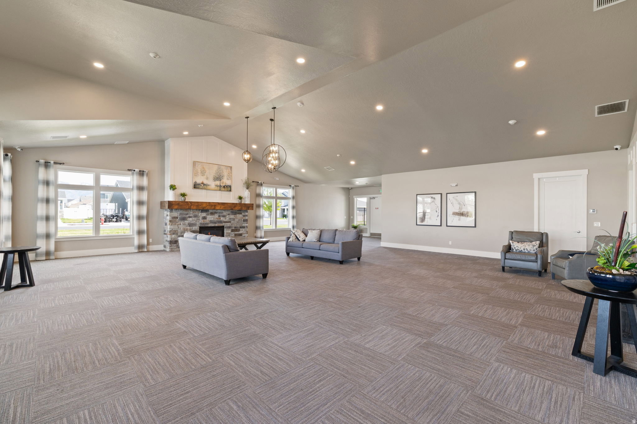 Spacious common area featuring a vaulted ceiling with recessed lighting, a stone-front fireplace with a wood mantle, and large windows
