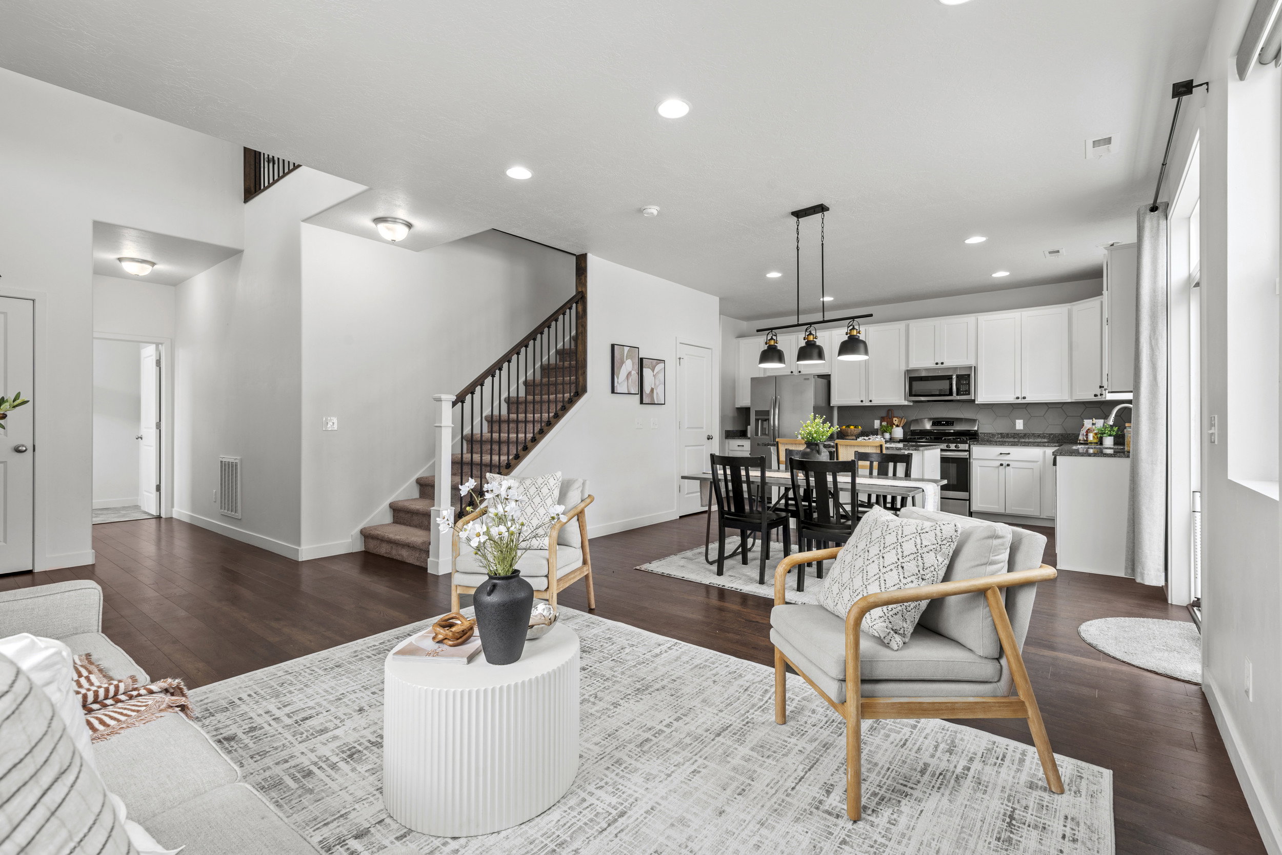 Open-concept living area featuring rich wood-finish flooring, a contemporary staircase with dark wood railings, and recessed ceiling lighting
