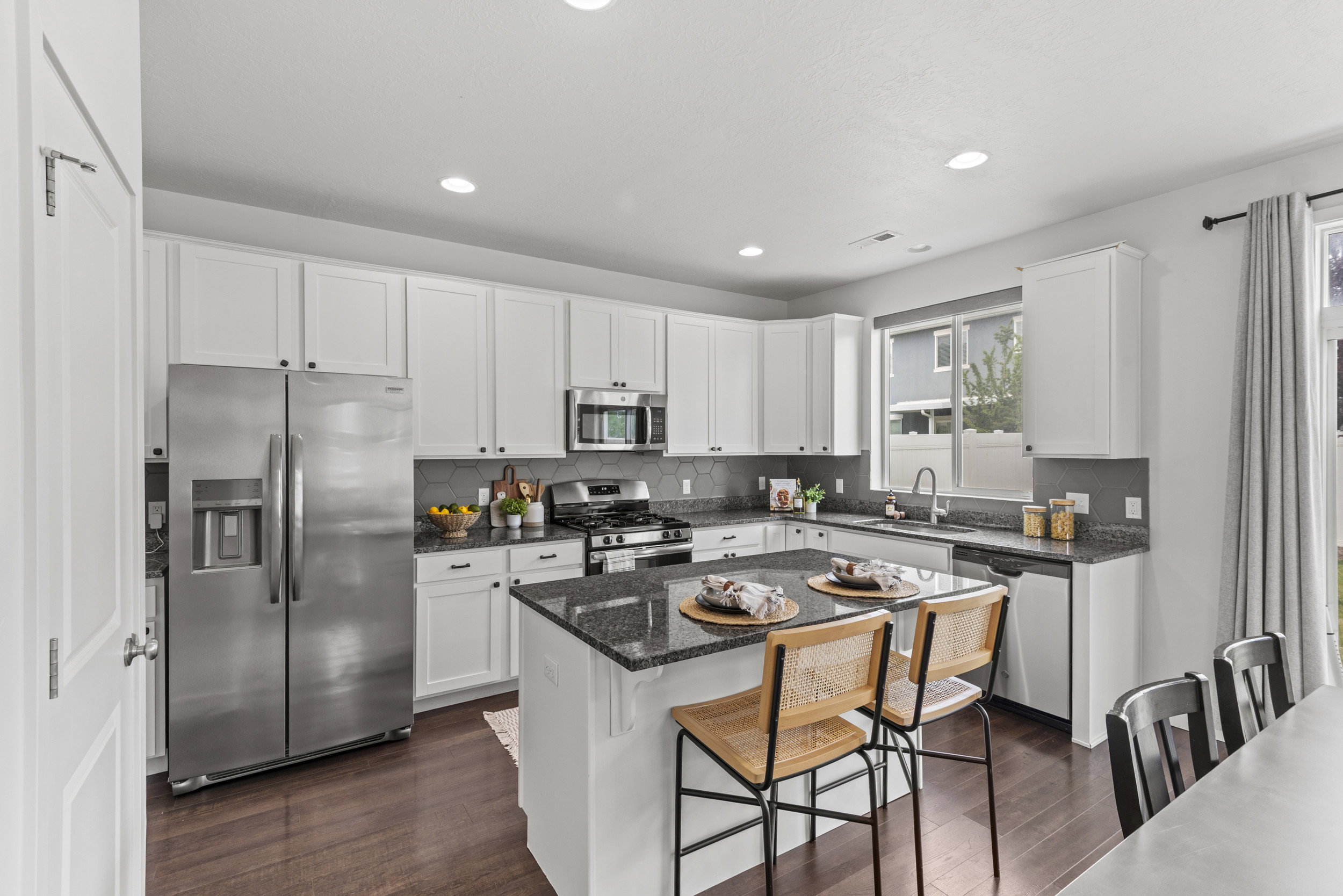 Modern kitchen featuring white shaker cabinetry, stainless steel appliances, dark granite countertops, a coordinating backsplash, and wood-finish flooring
