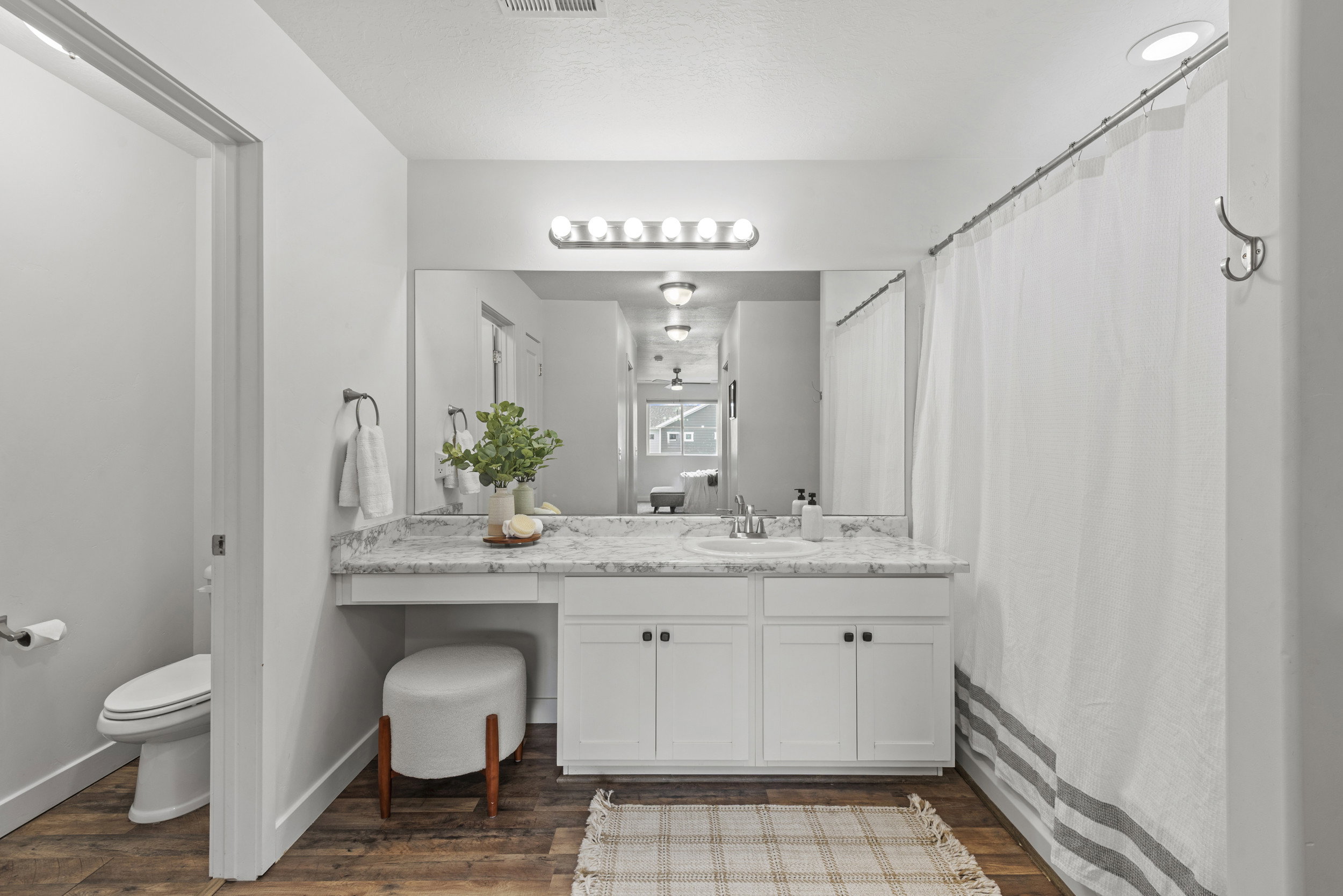 Bathroom featuring a white vanity with built-in storage, a light-toned countertop, a large mirror, a chrome-finish light fixture, and wood-finish flooring