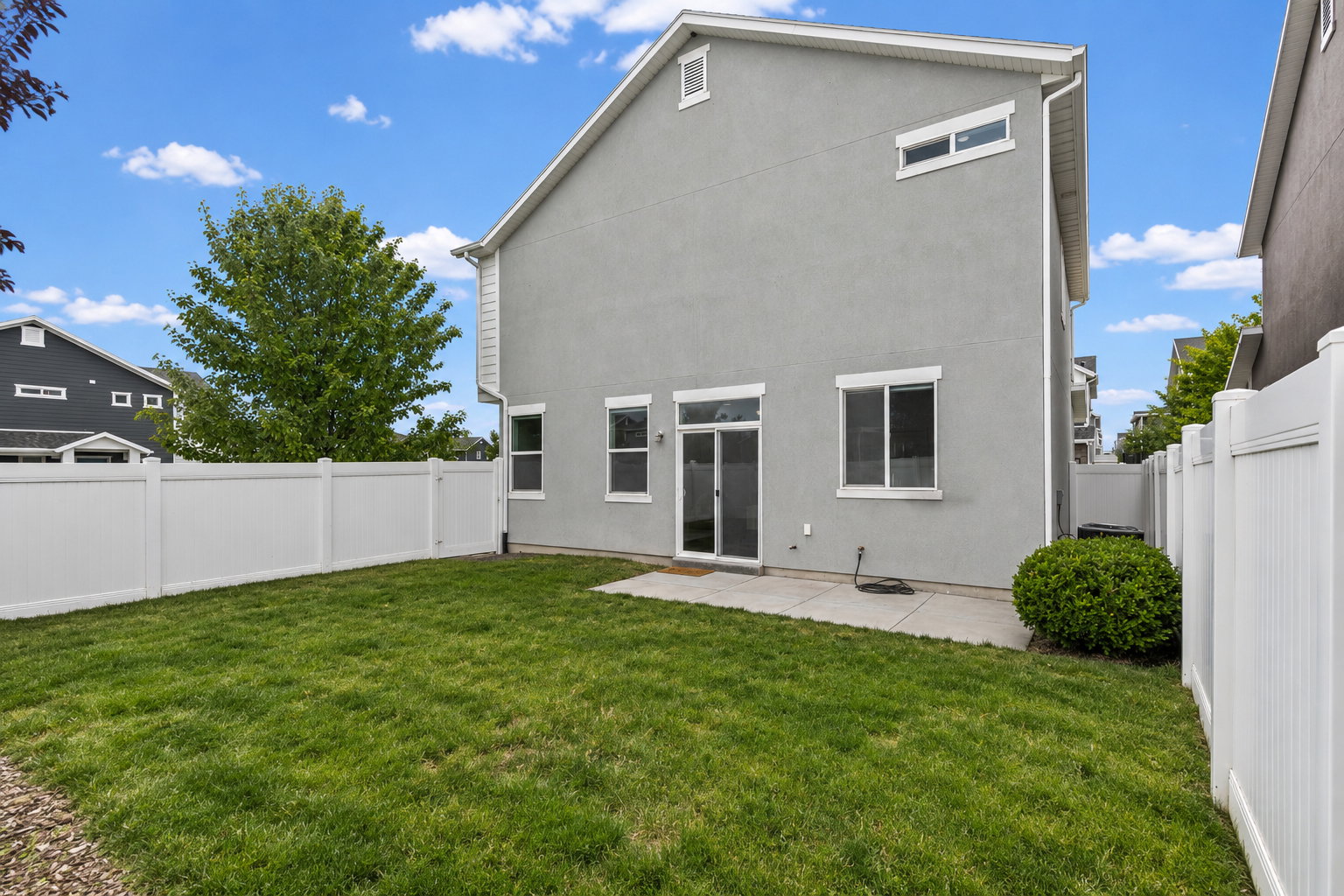 Expansive backyard featuring a manicured lawn, full vinyl privacy fencing, and a concrete patio