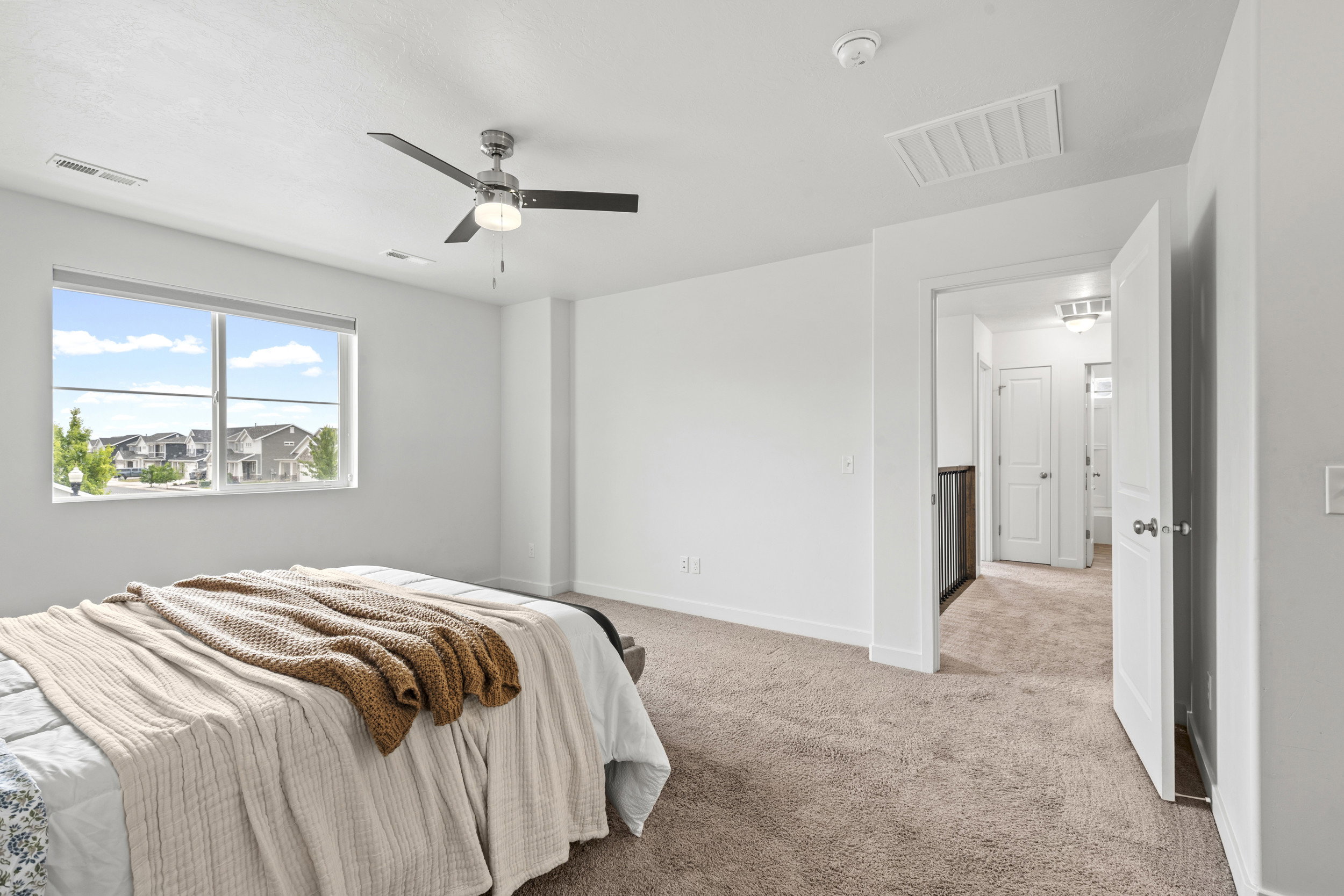 Spacious room featuring a large window, neutral carpeting, a modern ceiling fan, and white baseboards
