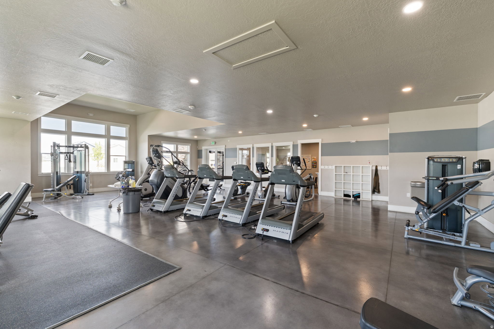 Dedicated fitness center featuring large windows, recessed lighting, polished concrete flooring, and built-in storage cubbies