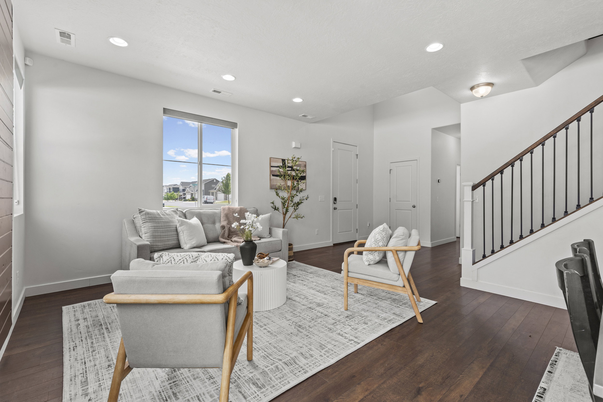 Living area featuring dark wood-finish flooring, a large window, recessed lighting, and a staircase with a dark wood handrail and black balusters