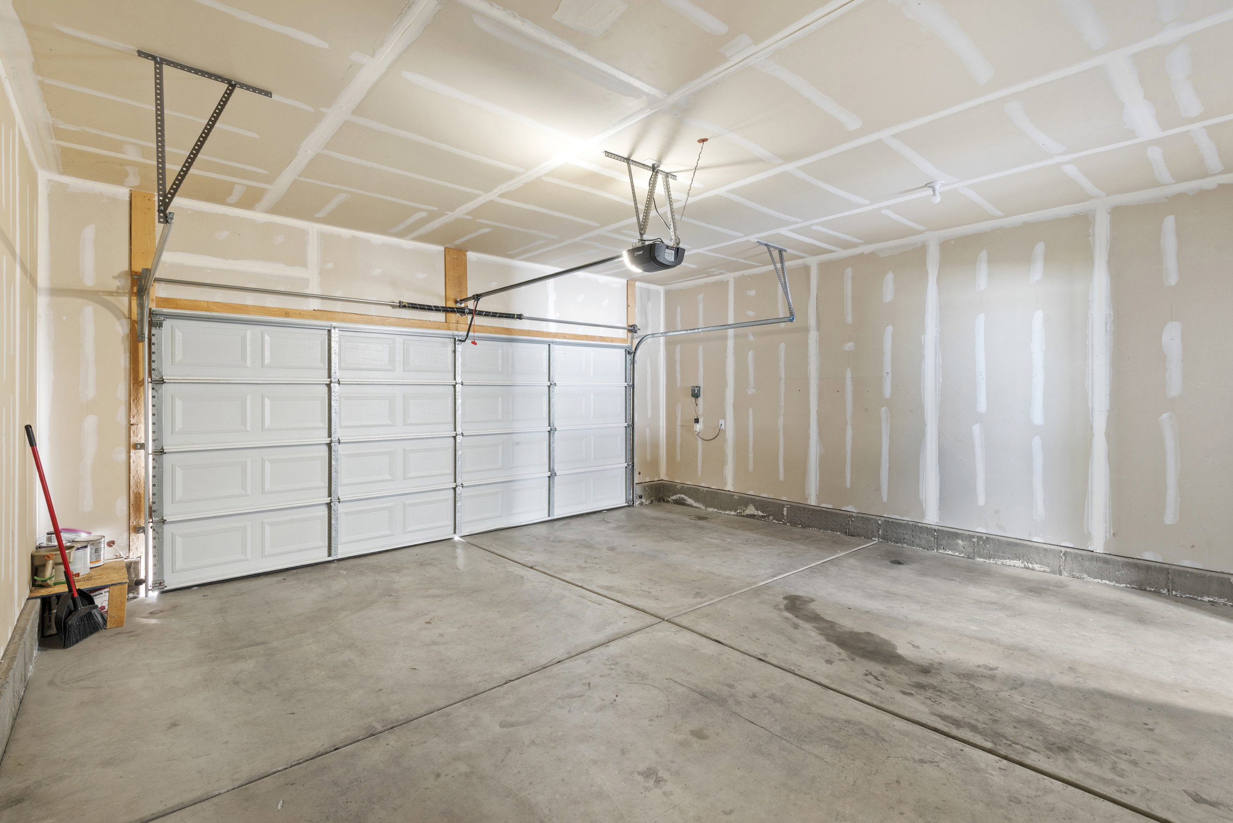 Spacious garage featuring a concrete floor, two white panel garage doors, and an exposed ceiling with an automatic opener