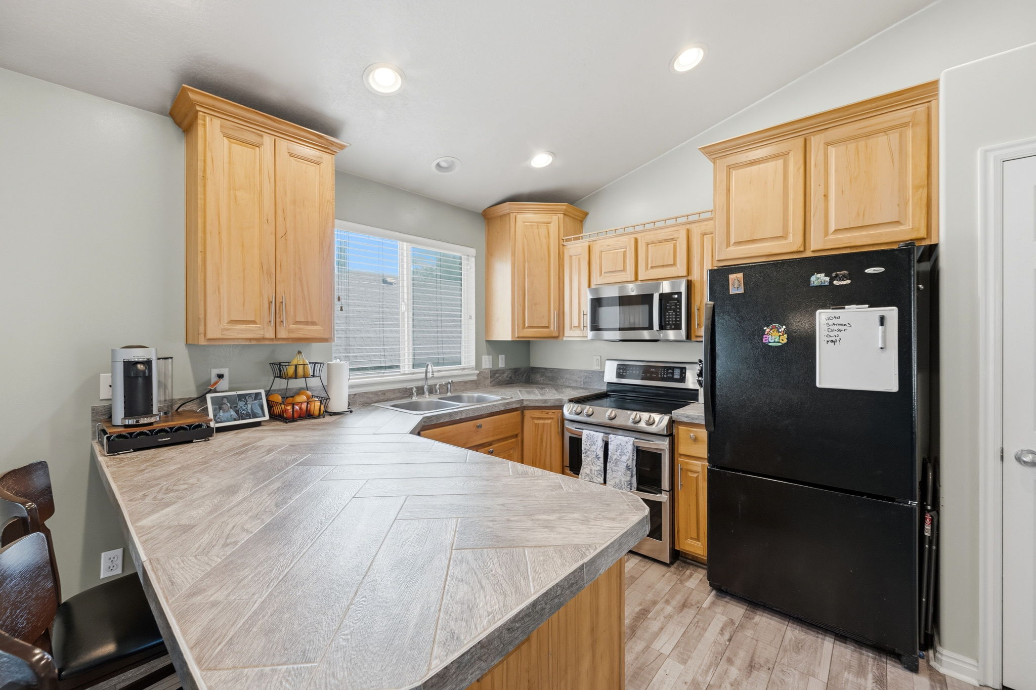 Kitchen featuring wood-finish cabinetry, stainless steel appliances, a corner double-basin sink, and a multi-level countertop with a herringbone pattern