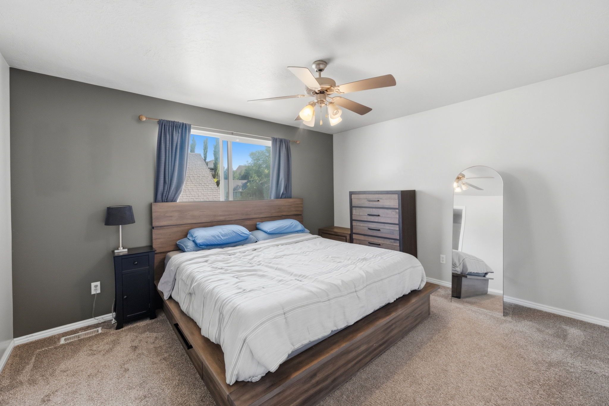 Carpeted bedroom featuring a large window, a ceiling fan with integrated lighting, and a neutral color palette with an accent wall