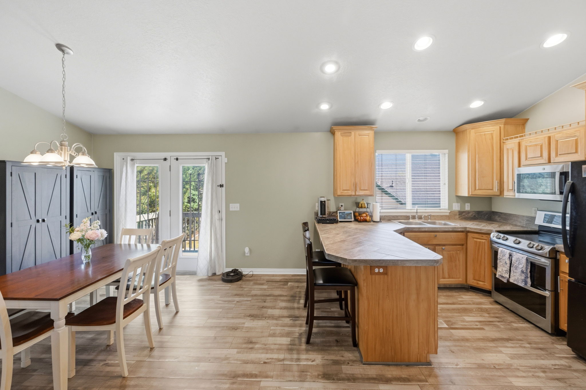 Open-concept kitchen and dining area featuring wood-finish flooring, light wood cabinetry, recessed lighting, and a kitchen island with a breakfast bar