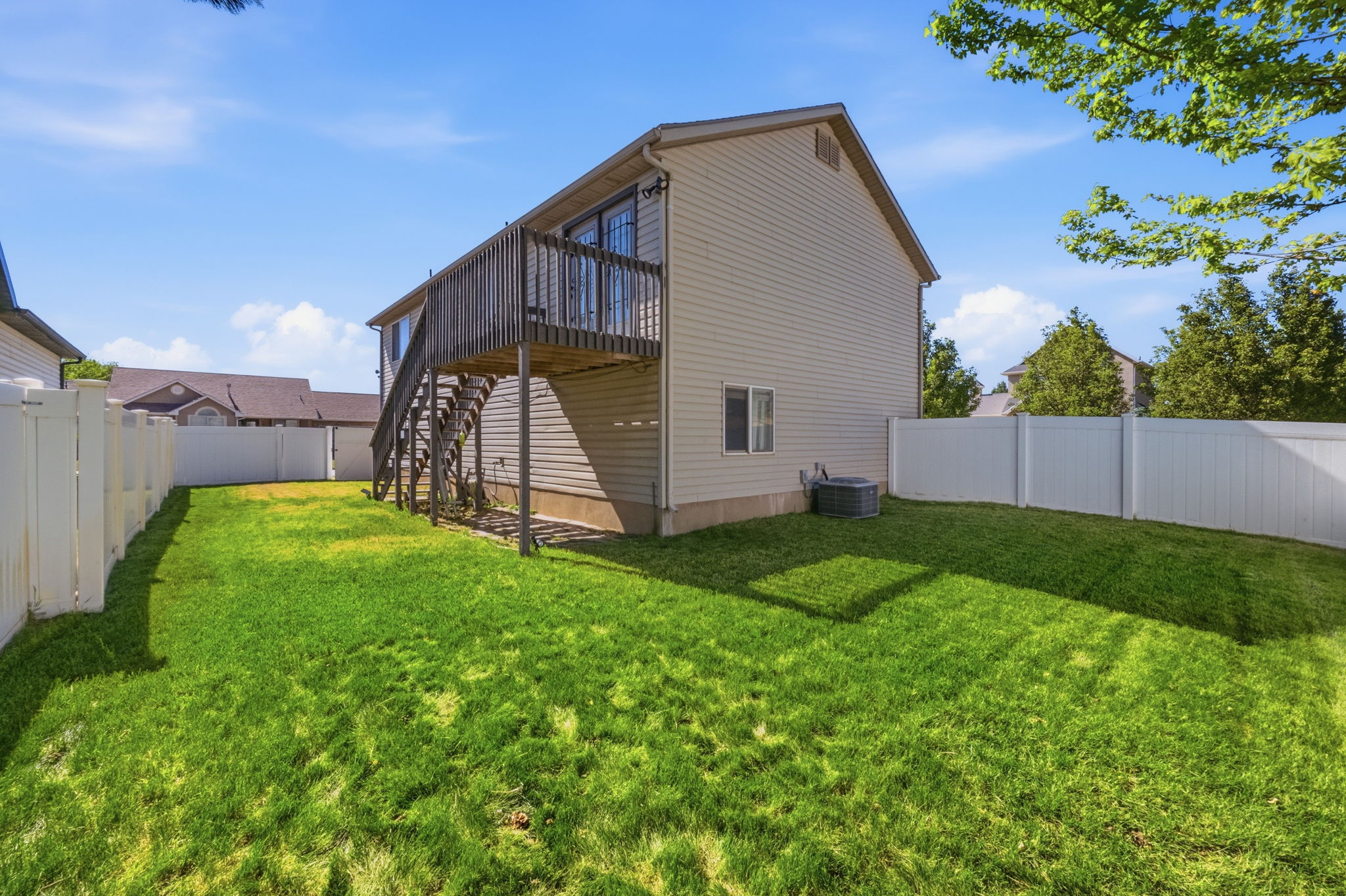 Rear exterior featuring a spacious green lawn, a privacy fence, and a raised wooden deck with stairs