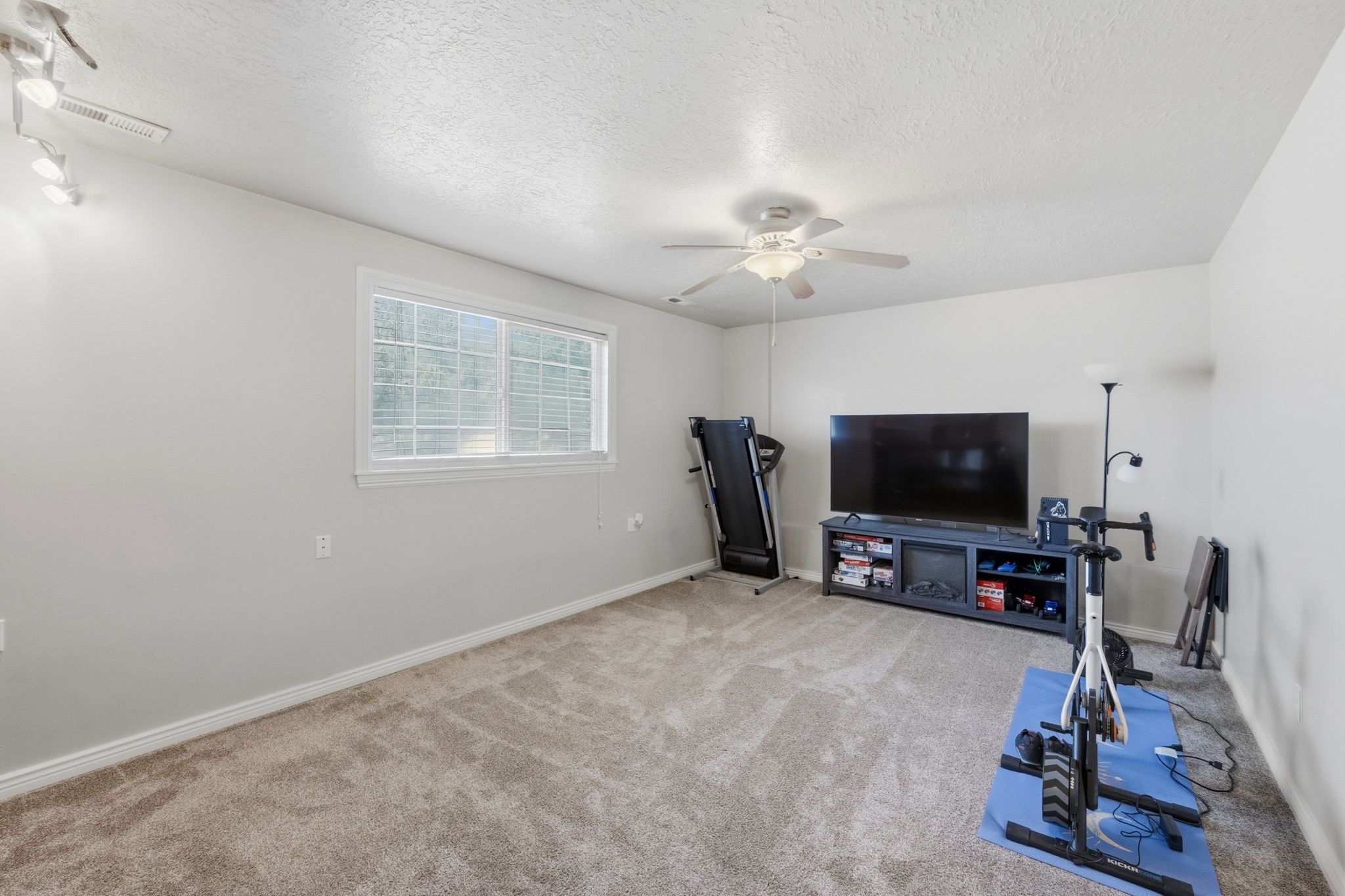 Spacious room featuring neutral carpeting, a large window with blinds, and white painted walls