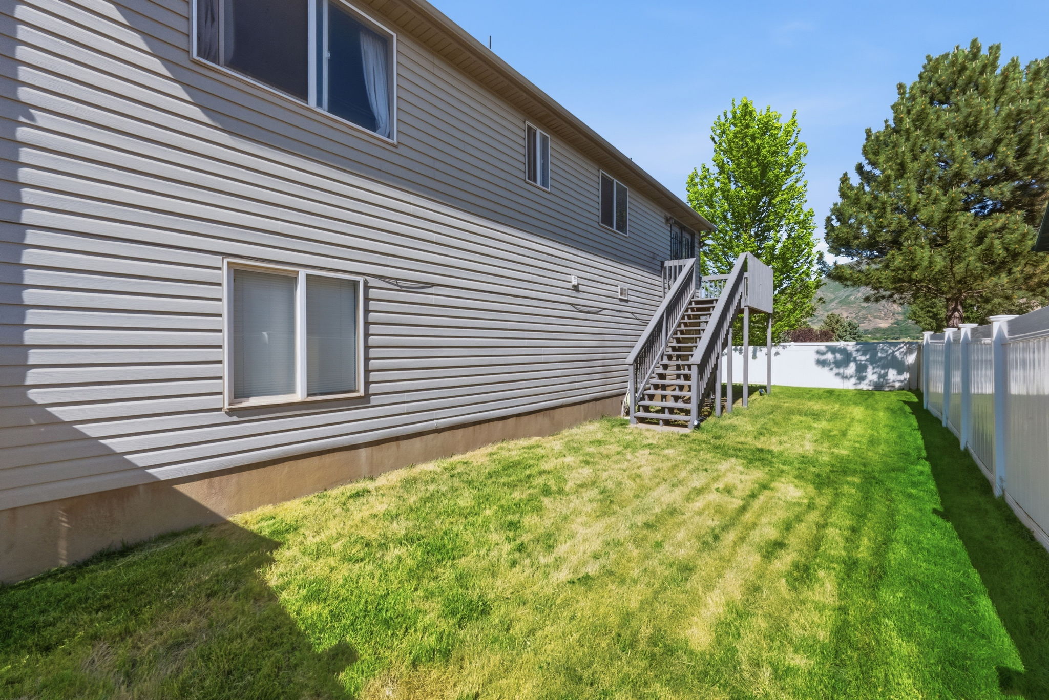 Expansive backyard featuring a manicured lawn, white privacy fence, and multi-level deck with exterior stairs