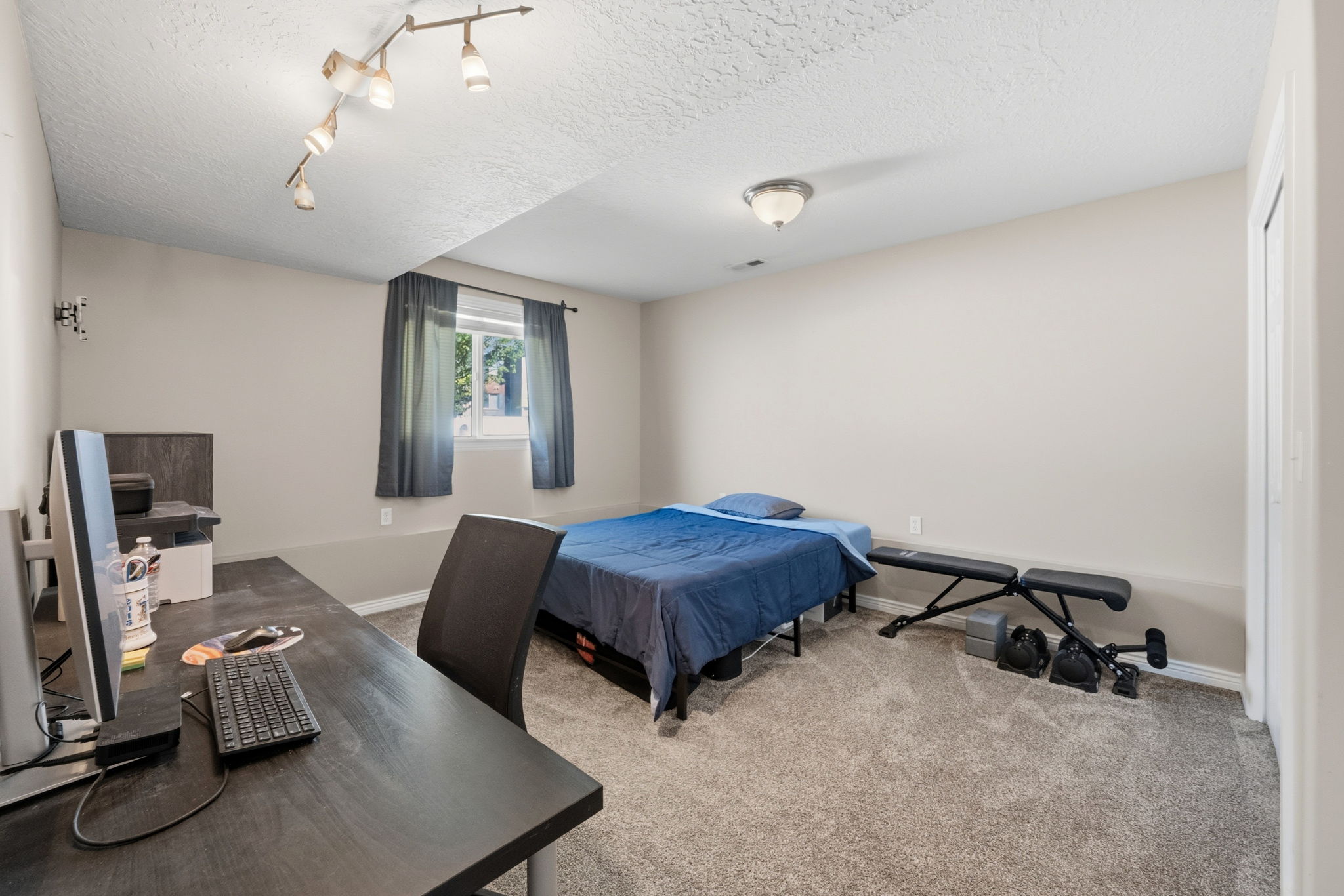 Bedroom featuring light gray walls, textured ceiling, a window with dark curtains, and plush carpet flooring
