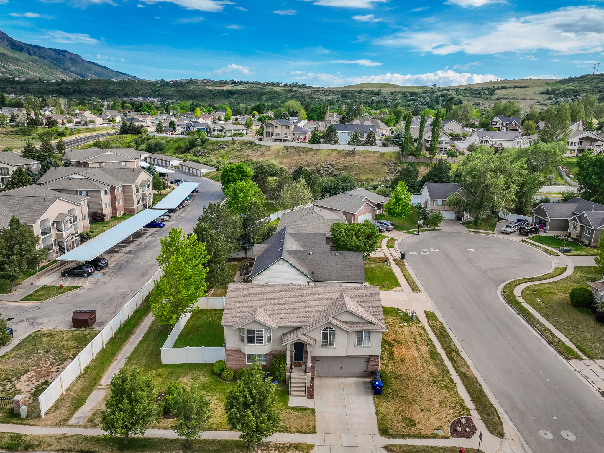 Split-level residence featuring a two-car garage, mature front yard trees, and a white fence enclosing a rear lawn