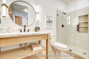 Bathroom featuring a wood-finish vanity with a stone countertop, a circular mirror, and a glass-enclosed shower with subway tile