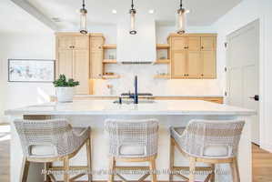 Kitchen featuring a large central island with a stone countertop, custom light wood cabinetry, a white tile backsplash, and three pendant light fixtures