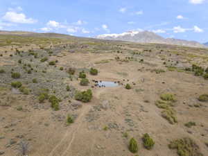 Expansive land parcel featuring a natural pond, diverse brush, and distant snow-capped mountains
