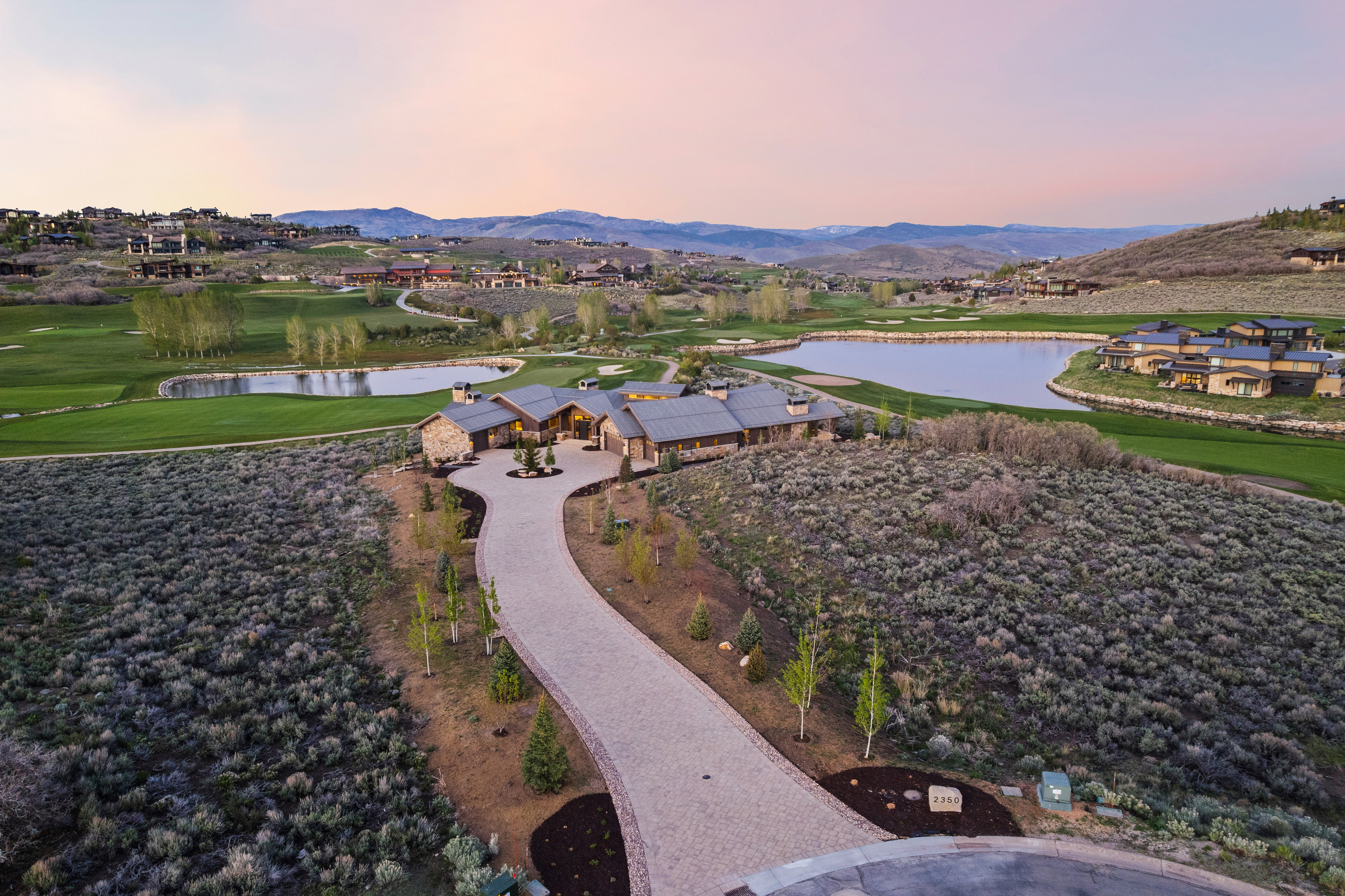 Expansive estate featuring a stone and wood facade, a long winding driveway, and a multi-car garage
