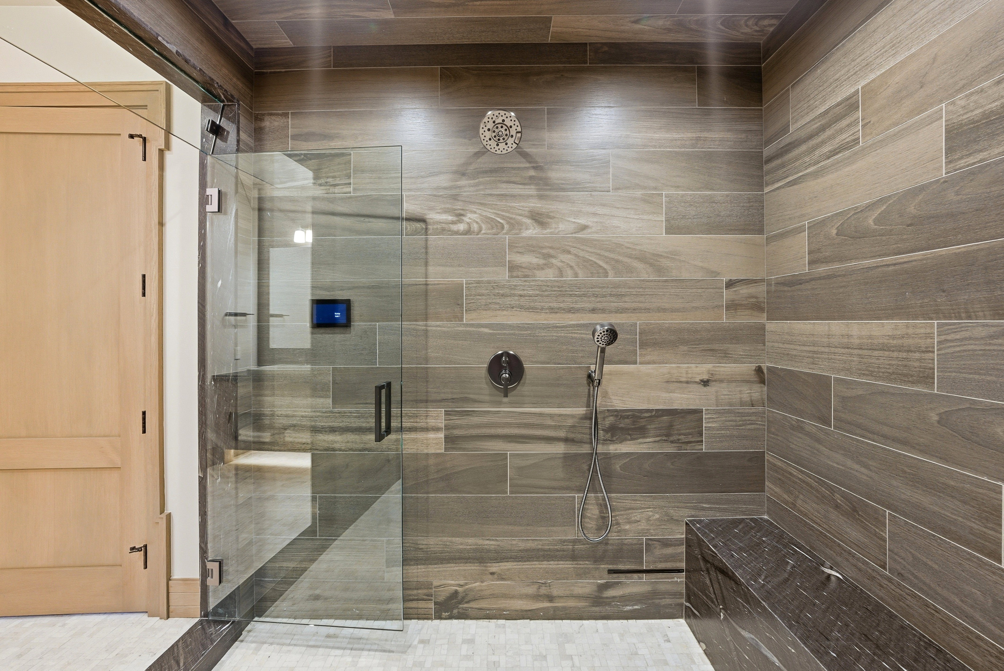 Walk-in shower featuring wood-finish tile walls, glass enclosure, built-in stone bench, and rain shower head