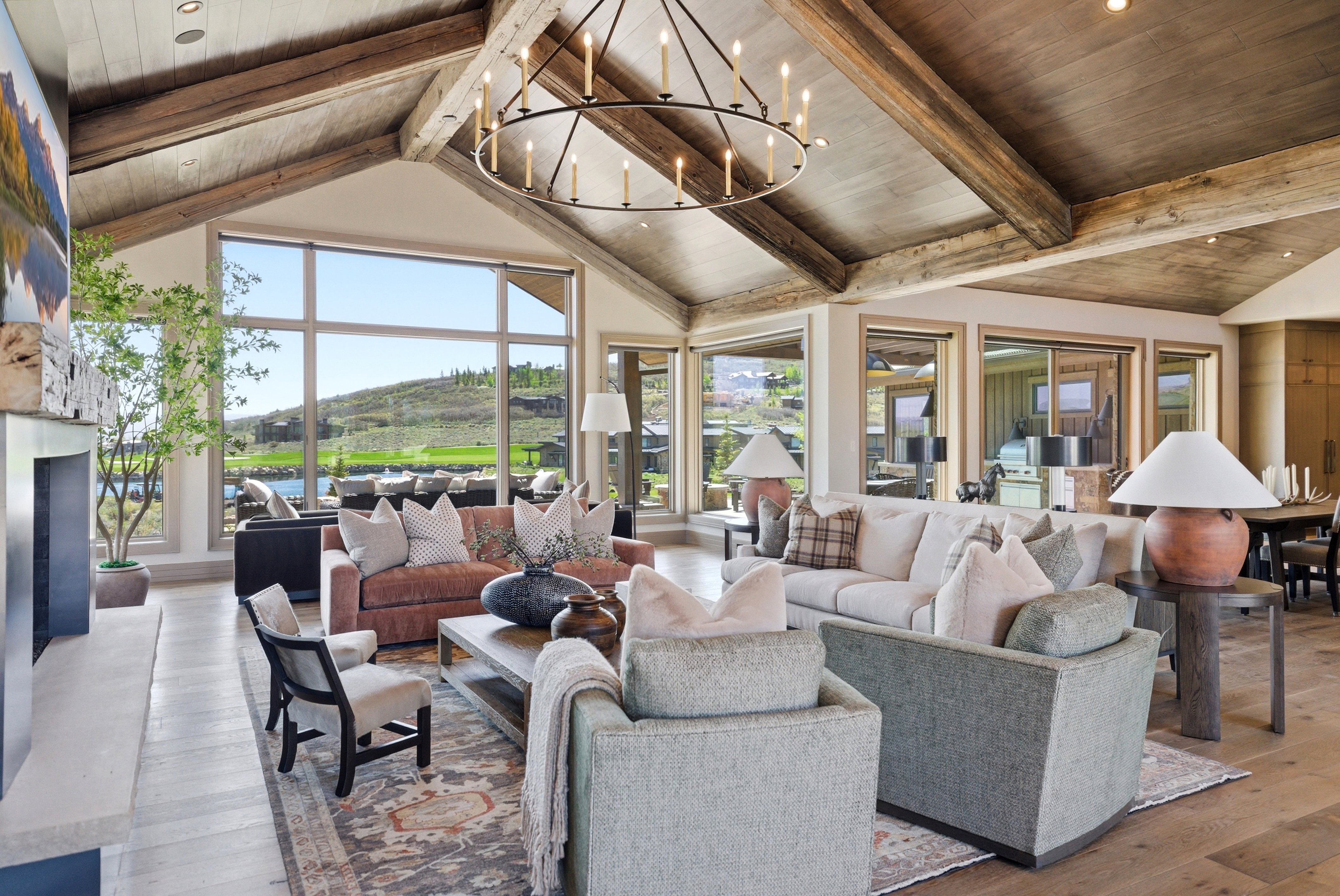Spacious living area featuring a vaulted wood-beam ceiling, a large iron chandelier, and a stone-clad fireplace