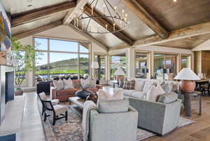 Spacious living area featuring a vaulted wood-beam ceiling, a large iron chandelier, and a stone-clad fireplace