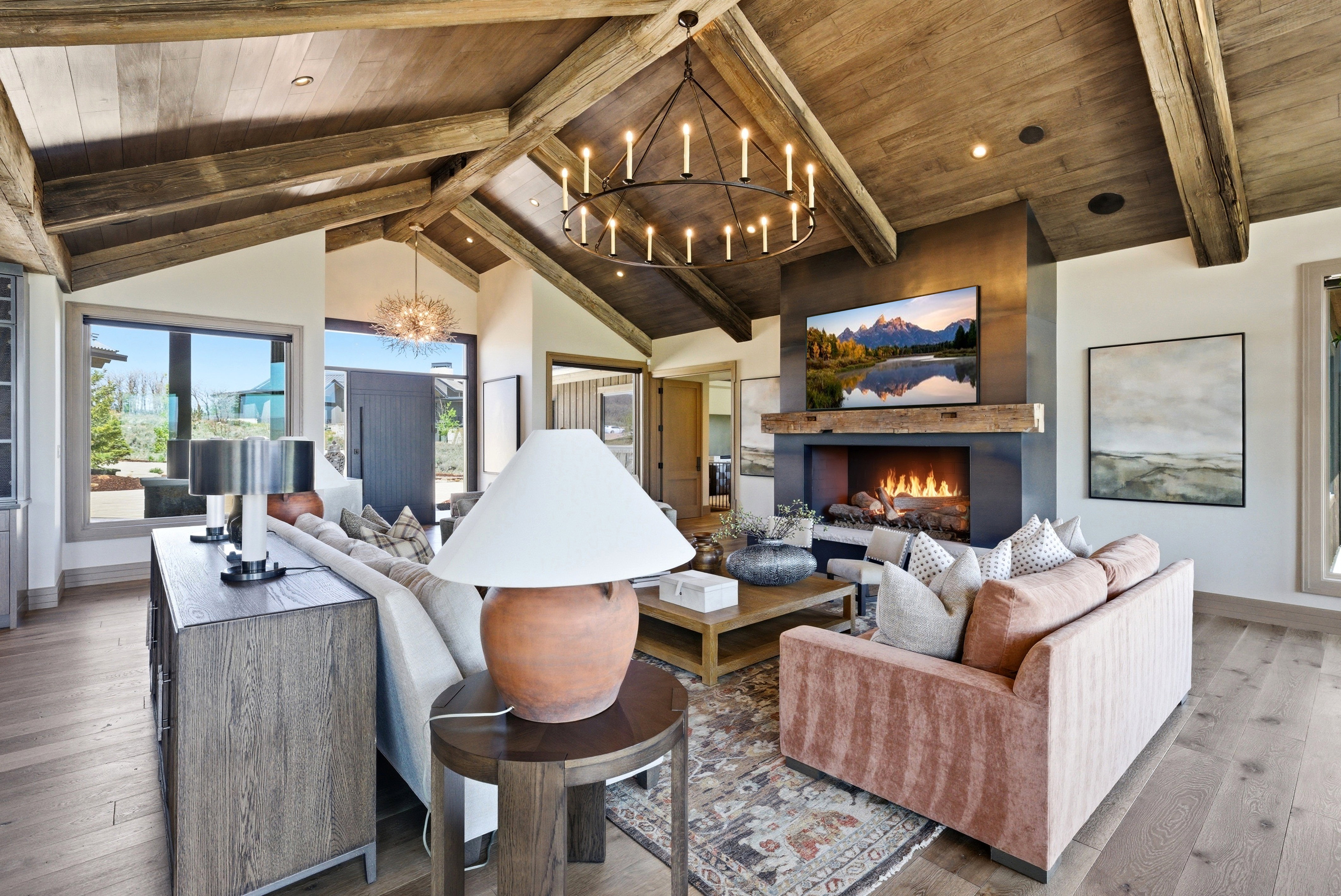 Vaulted wood-paneled ceiling with exposed beams, central fireplace feature with a wood mantel, wide plank wood-finish flooring, and large windows