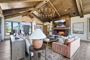 Vaulted wood-paneled ceiling with exposed beams, central fireplace feature with a wood mantel, wide plank wood-finish flooring, and large windows