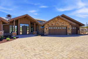 Contemporary-rustic exterior featuring a paver driveway, natural stone accents, wood siding, a metal roof, and multiple garage doors