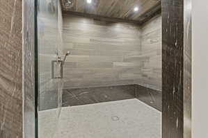 Walk-in shower featuring a glass enclosure, a built-in bench with dark stone, light wood-finish ceiling, and light tile walls