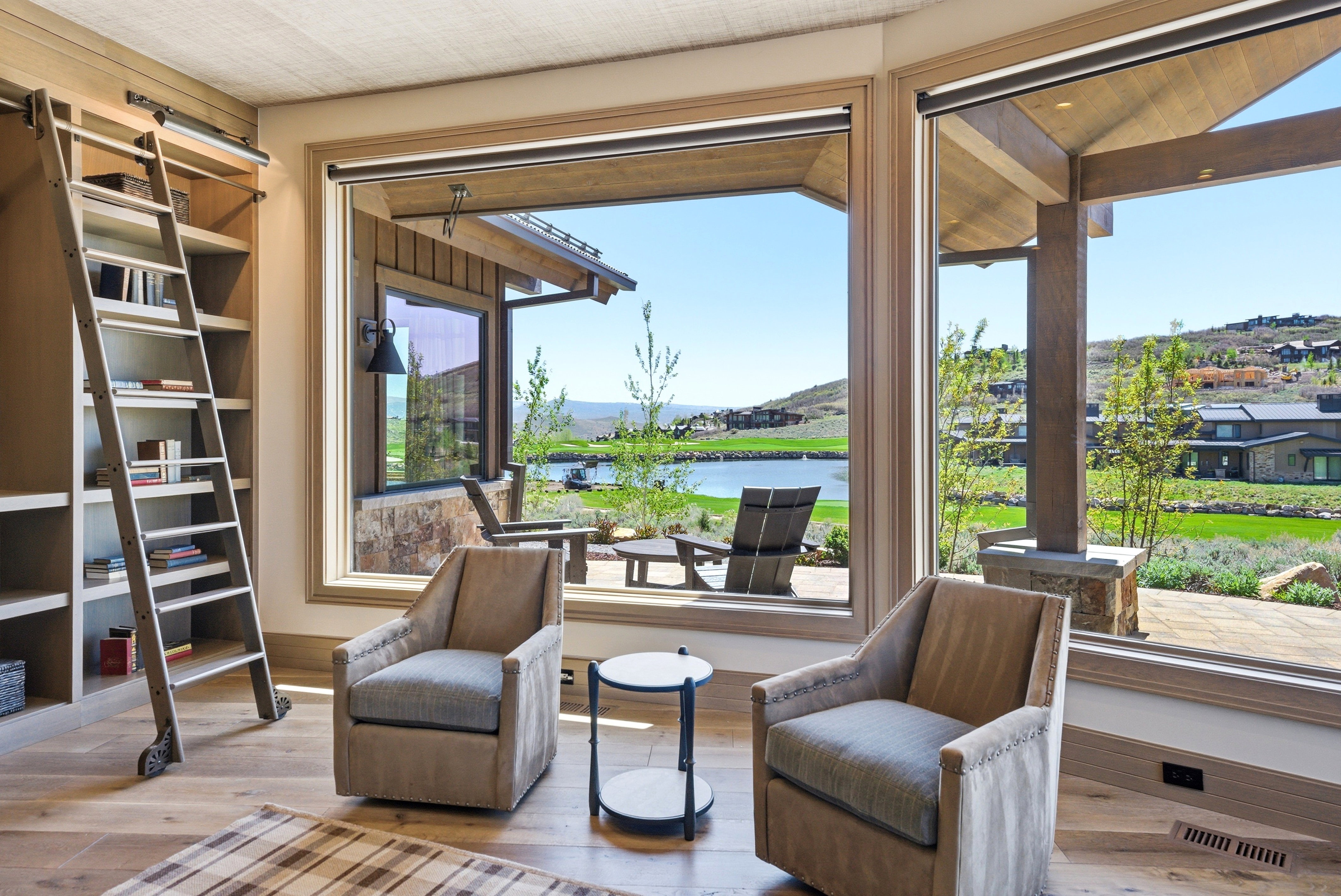 Expansive windows overlooking a lake, built-in shelving with a rolling ladder, wood-finish flooring, and a natural wood ceiling