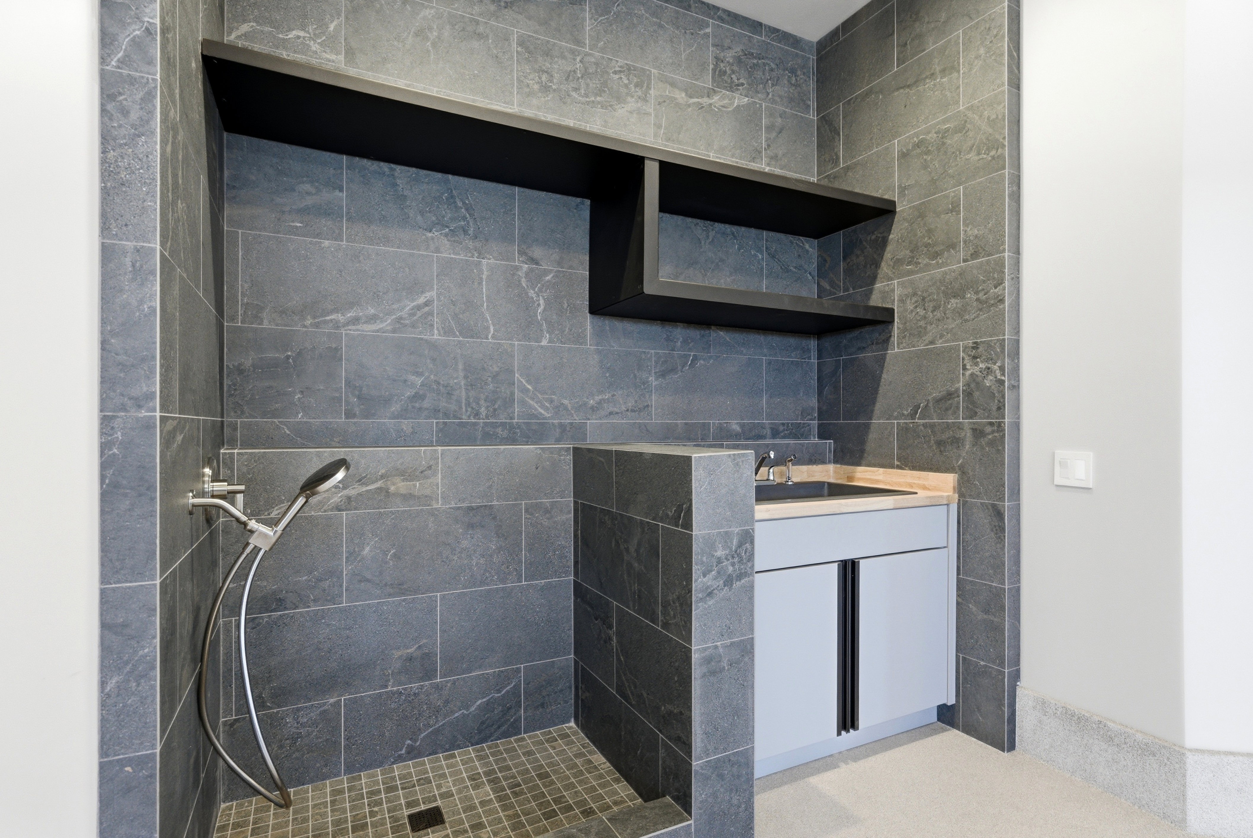 Shower area featuring full-height dark stone-look tile, a handheld shower fixture, and a tiled shower pan