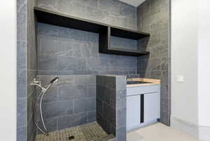 Shower area featuring full-height dark stone-look tile, a handheld shower fixture, and a tiled shower pan