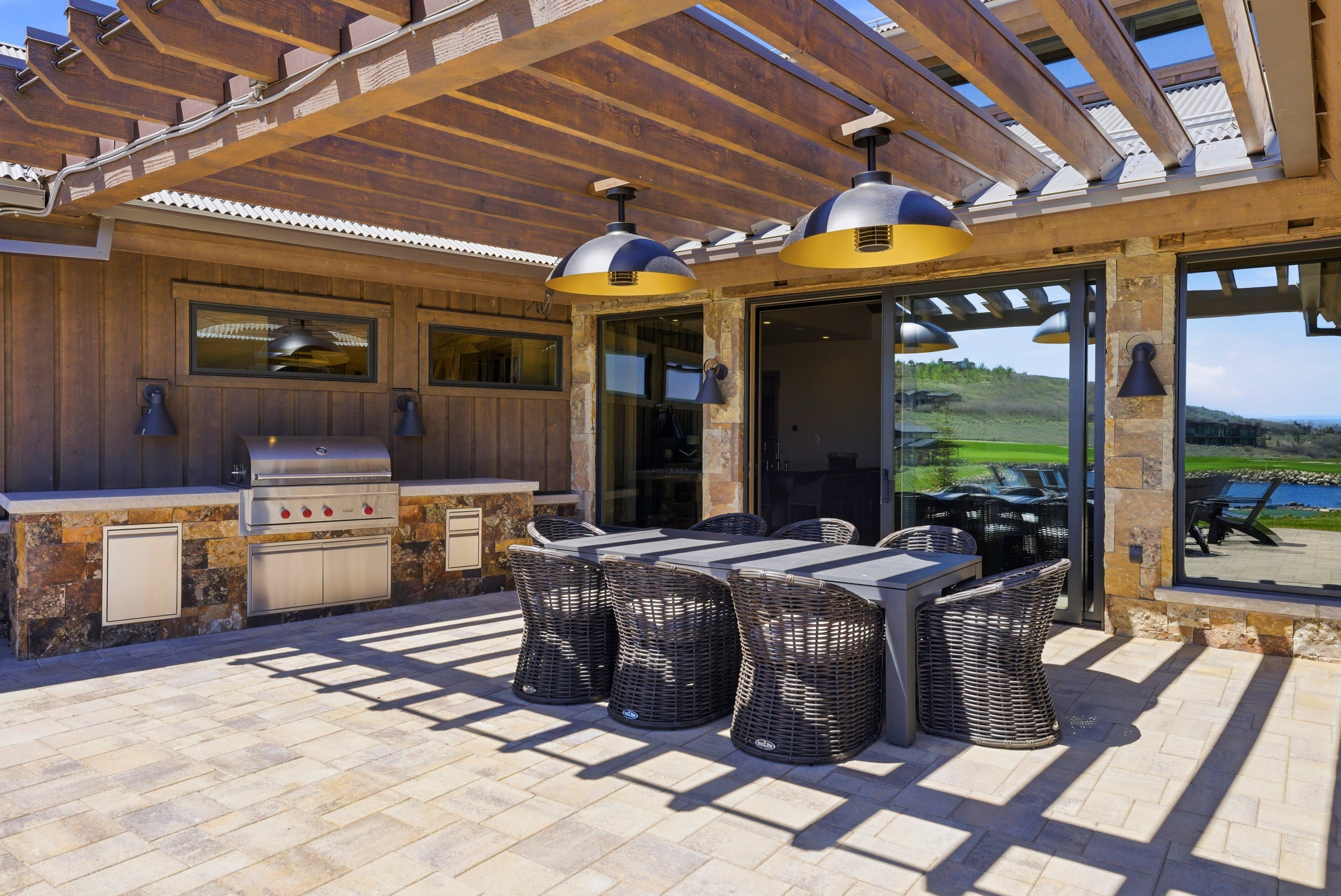 Outdoor patio featuring a built-in stainless steel grill, stone veneer base, and a wood pergola with integrated lighting